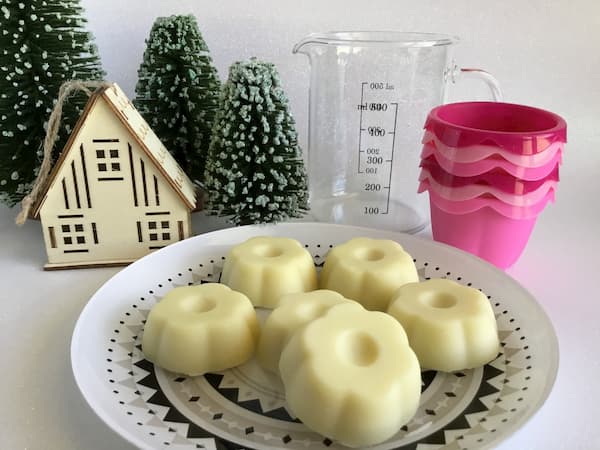 six flower-shaped lotion bars sitting on a plate with ikea baking cups and glass measuring jug in background