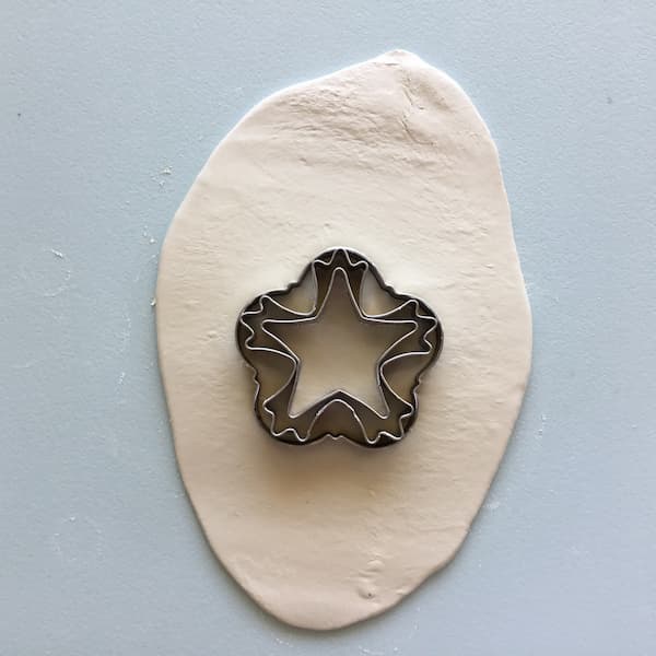 white clay rolled out on a blue board with three nested snowflake cookie cutters sitting on top