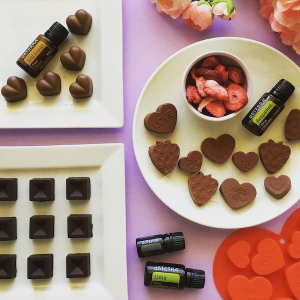 valentine's chocolates laid out on plates with flowers, freeze dried strawberries, a heart silicone mold and bottles of doterra essential oils