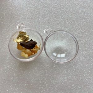 a small clear plastic bauble in two halves and one half contains pieces of gold, frankincense and myrrh