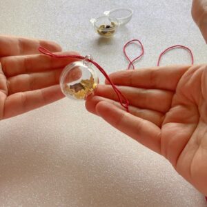 a pair of hands showing a bauble with looped embroidery thread pulled half way through