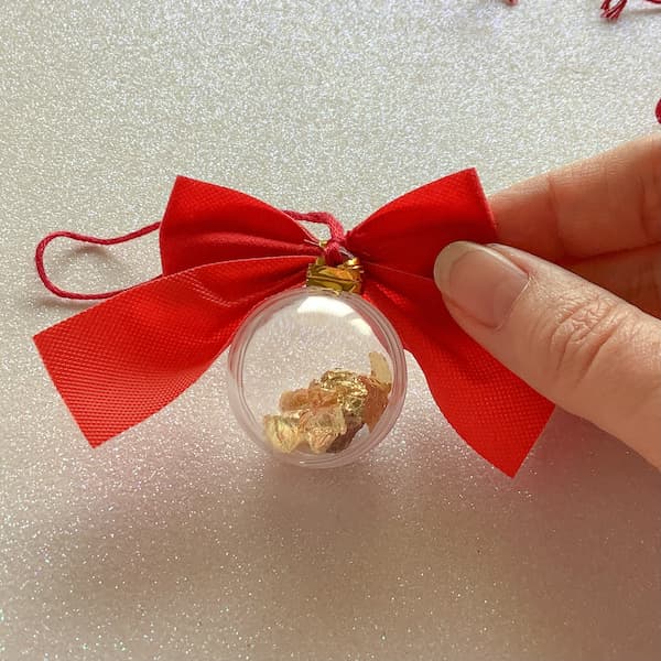 a hand holding a bauble showing how the tie of a red bow has been wrapped around the bauble to attach it