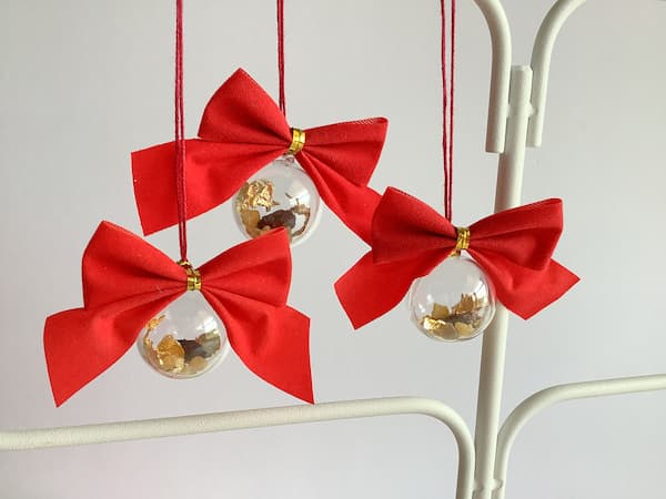 three clear baubles with red bows and gold, frankincense and myrrh pieces inside hanging from an ornament stand