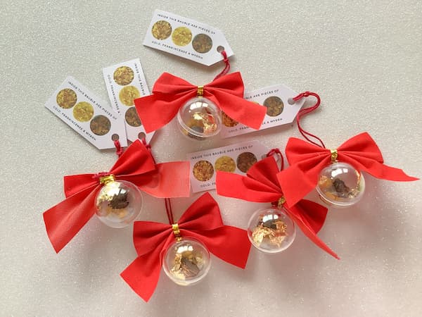 5 christmas ornaments with red bows and tags lying on a white, glittery backgound